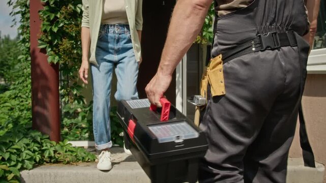 Unrecognizable handyman carrying toolbox walking toward house entrance to meet female homeowner. Footage suitable for home repair, maintenance and plumbing service promo