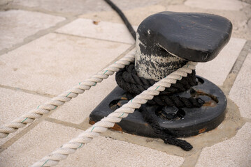 Fototapeta premium Cast iron mooring bollard with ropes on stone pier in morning harbor.