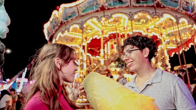 Romantic young couple eating cotton candy at night amusement park