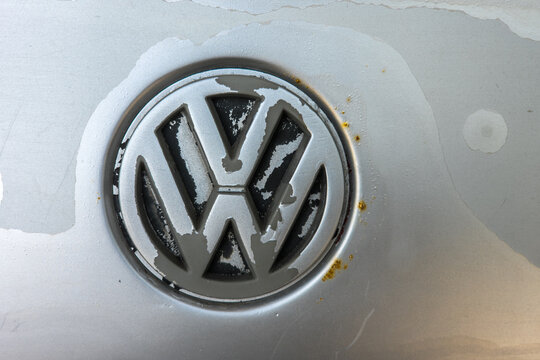 Bishkek, Kyrgyzstan - June 9, 2025: A close-up view of a weathered Volkswagen emblem on a silver vehicle body. The emblem shows signs of wear, including peeling paint and corrosion, with water marks