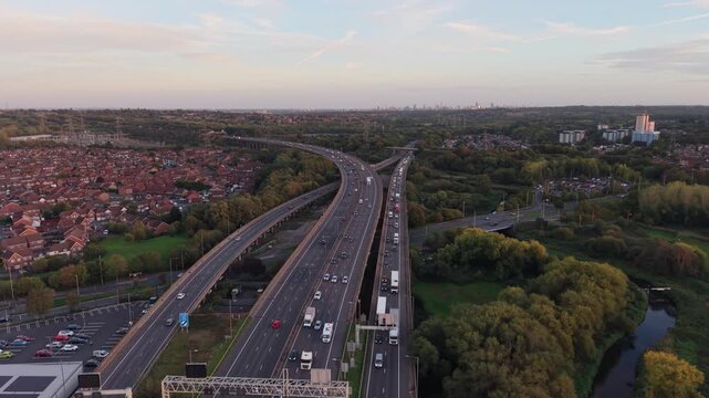 Aerial drone flight over the M6 and M5 motorway interchange in England at sunset, showing busy traffic, merging lanes, slip roads, cars and trucks travelling through a major British transport corridor