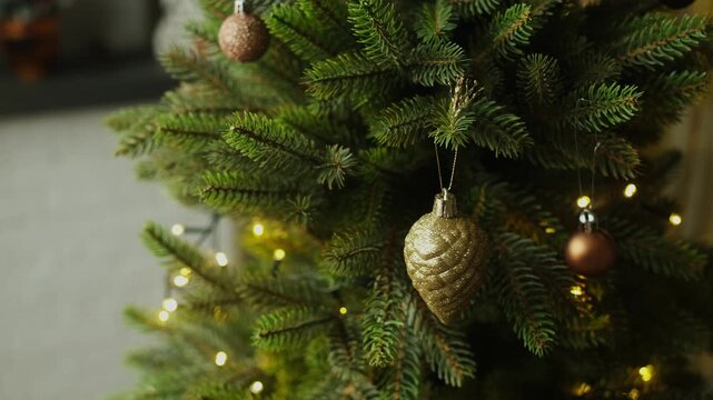 Female hands decorating Christmas tree, hanging golden Christmas ornaments.