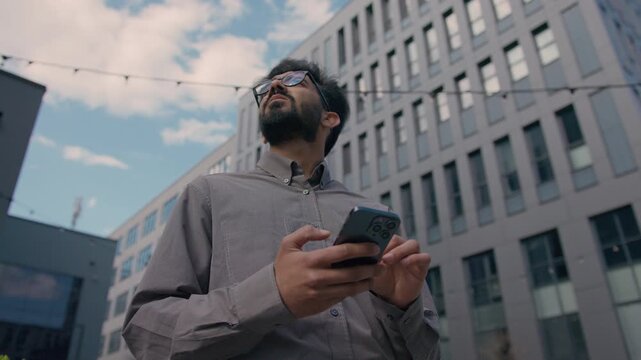 Confused Indian Arabian business man tourist checking GPS map smartphone outdoors in city male businessman looking around for location navigation lost traveler searching street using geolocation apps