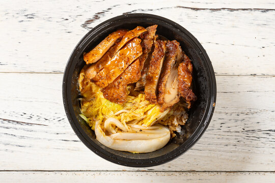 Grilled chicken rice bowl with napa cabbage served in black plastic takeaway container