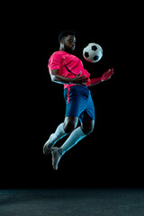 Black male footballer jumping to control ball with chest in dark studio with focus. Technique tutorials, athletic conditioning concept. © master1305