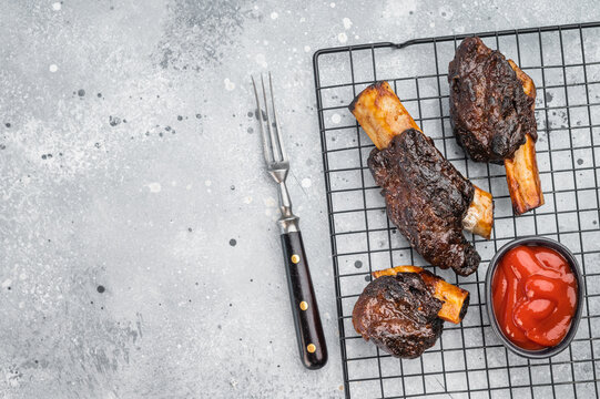 Slow cooked beef short ribs with bone and BBQ sauce on grill rack. Tender braised beef ribs plate style on light background.