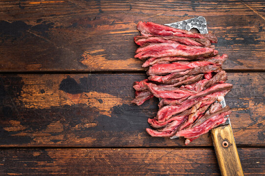 Sliced grilled machete skirt steak arranged on rustic cleaver knife over wooden background top view barbecue style with copy space