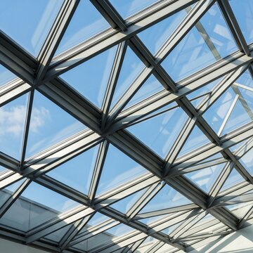 Modern glass roof structure with geometric design and blue sky  
