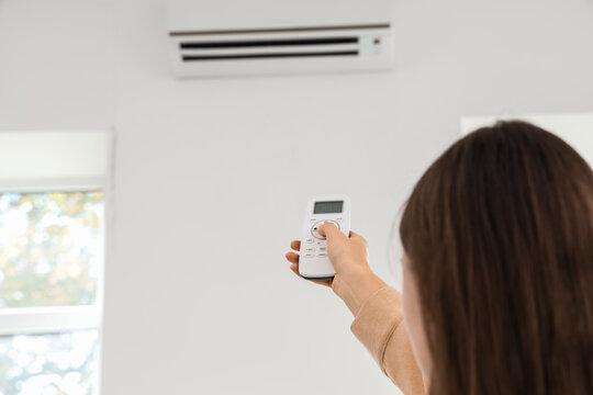Climate control and energy efficiency, woman using remote to adjust air conditioning temperature for home comfort and cooling in a modern living room