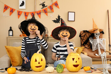 Fototapeta premium Halloween celebration, children in witch and wizard costumes holding paper jack-o-lantern masks while carving pumpkins at home for a festive party