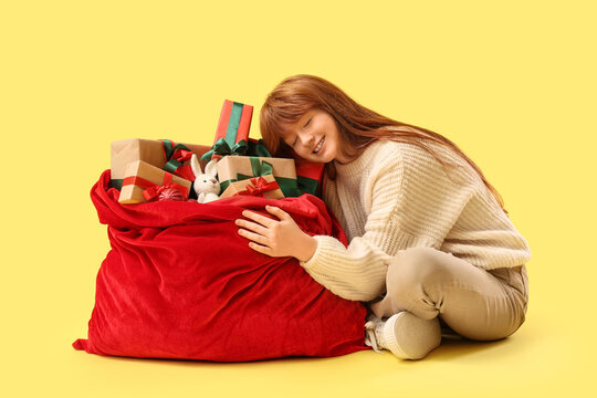 Christmas joy and holiday spirit, happy girl hugging a large red sack full of wrapped gifts and presents on a yellow background