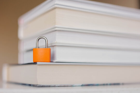 Orange padlock securing a stack of books, symbolizing censorship, restricted information, freedom of speech, and limitations on access to knowledge.