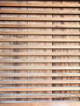 Close-up of weathered wooden latticework with horizontal slats over vertical boards, showing aged wood grain, a small metal nail, and a repeating linear pattern.

