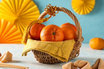 Fototapeta premium Lunar New Year celebration, fresh mandarin oranges in a wicker basket with traditional gold tassel and paper fans for prosperity and good fortune
