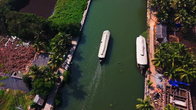 High angle drone shot of a houseboat cruising on a palm-fringed canal in India