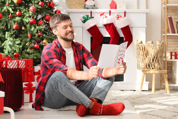 Christmas greetings and holiday joy, happy man reading a festive card at home with a decorated tree and fireplace in a cozy winter living room © Pixel-Shot
