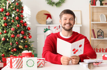 Christmas greetings and holiday traditions, happy man reading festive card at home with decorated tree and gifts for winter season celebration © Pixel-Shot