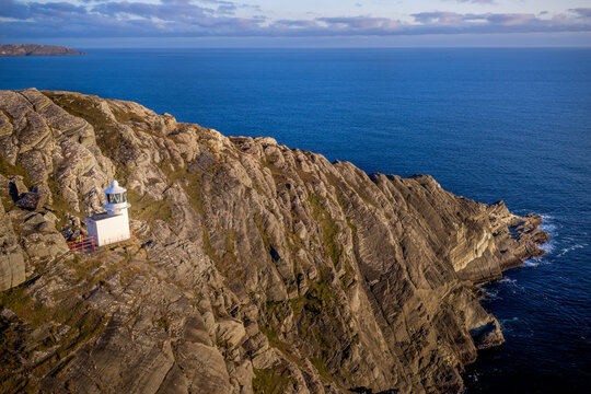 Aerial view of white Sheep's Head Lighthouse perched on rugged rocky cliffs overlooking  Atlantic Ocean in County Cork, Ireland.