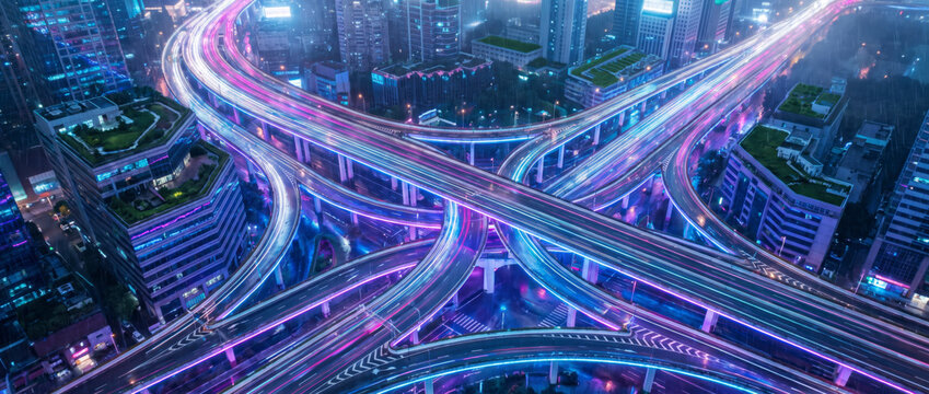 Aerial neon highway interchange with green roof office buildings in futuristic downtown at night