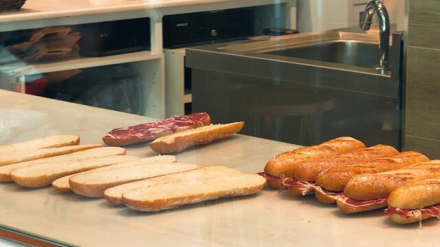 Worker in gloves assembling bocadillo sandwiches with jamon on baguette bread, Spanish fast food preparation footage. High quality 4k footage