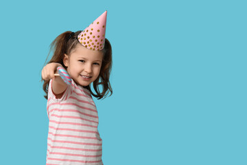 Fototapeta premium Birthday celebration and childhood joy, happy little girl wearing a party hat holding a colorful lollipop on a solid blue background