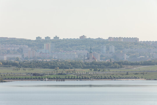 01 October 2026, View across Lake Most towards the smoggy city skyline and historic church, Most, Czech Republic.
