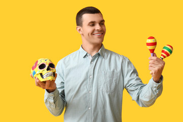 Fototapeta premium Dia de los muertos celebration, man holding traditional sugar skull and maracas for mexican holiday festival and cultural heritage event on yellow background