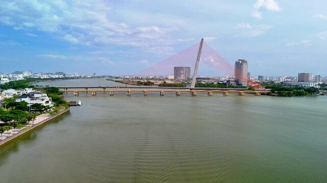 Majestic drone flight gliding above the calm Han River waters toward the graceful Tran Thi Ly Bridge with the bustling coastal city of Danang in the background