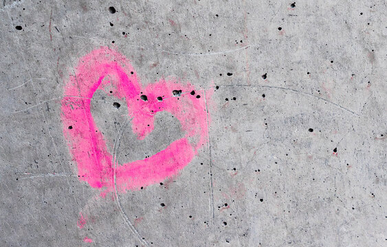 Neon Pink graffiti heart on rustic grey concrete stone texture wall with scratches