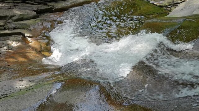 Mumlava cascades flow over smooth rock slabs in the Giant Mountains. Waterfalls and rapids shape the mountain stream.