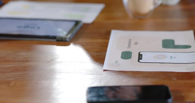 Camera is reframing upward, bringing tablet and mockups into focus as team is reviewing product
