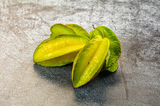 Grey stone surface with sliced green and yellow carambola star fruit pieces, tropical exotic fruit