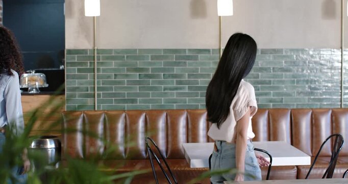 Mid-Adult diverse women entering left, pulling chairs, sitting at white table, meeting for coffee