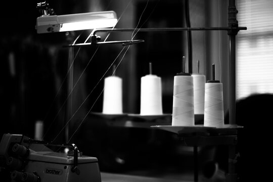 Thread cones on industrial sewing machine stand in dark tailoring workshop, black and white
