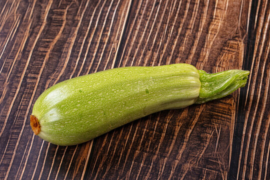 Fresh green zucchini squash resting on dark brown wooden plank surface with visible grain texture in rustic kitchen setting showing healthy vegetable