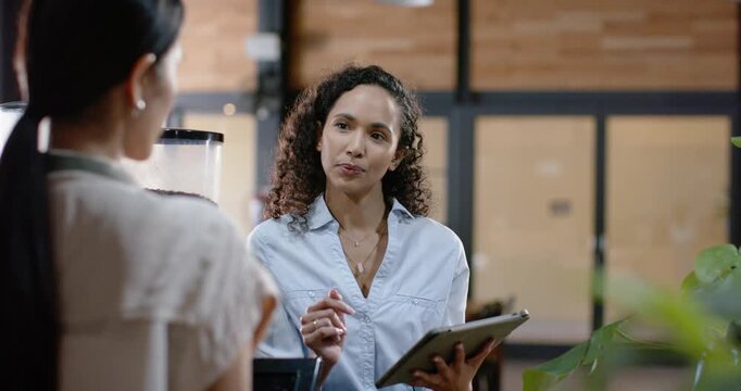 African American manager in blue shirt referencing tablet and training Asian barista at counter