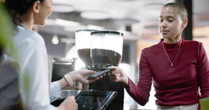 African American female customer and female barista passing cell tapping reader and paying at cafe