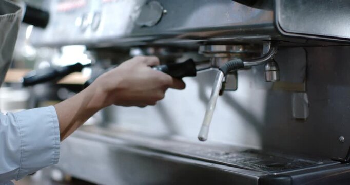 Barista hands are gripping portafilter then locking it and twisting knob to start espresso at cafe