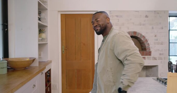 African American man leaning at kitchen island glancing down checking smartwatch for time laughing