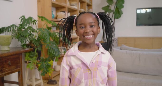 African American child in plaid smiling waving greeting camera moving closer at home near sofa