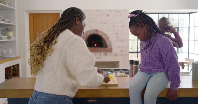 African family cooking in kitchen, white-sweater woman chopping yellow pepper, girl reaching lid