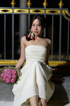 Elegant young woman in strapless white dress holding pink bouquet in outdoor setting