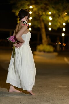 Woman Standing Outdoors at Night Holding Flowers in a White Dress, Night Scene, Warm Lighting