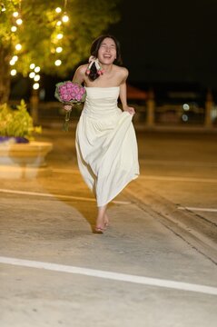 Joyful bride walking outdoors at night holding a bouquet of pink flowers