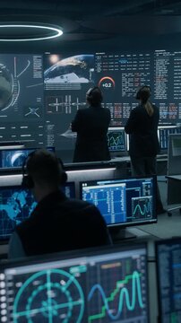 Vertical Screen. Monitoring Control Room. Team of Engineers in Headsets Review Earth Observation Feeds, Space Station Schematics, Flight Paths and Streaming Mission Data on a Command Wall.