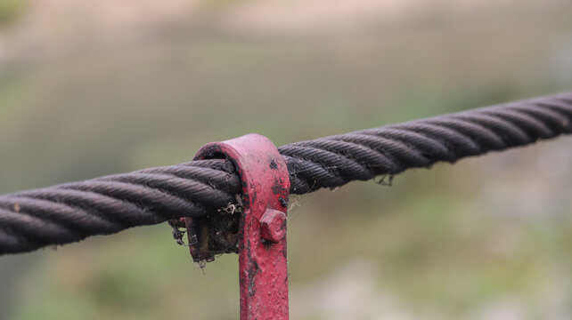 Industrial steel wire rope cable with red metal clamp bracket on a suspension bridge representing strength and structural engineering connection