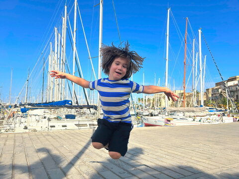 Yachting with children. A boy jumps with joy in the marina near sailing boats, enjoying a sea voyage around the islands. A child in a sailor t-shirt, a young captain