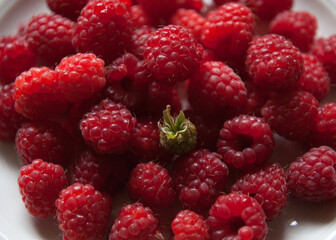 Red Ripe Raspberries with One Unripe Green Raspberry on a White Plate © PixelHarbor