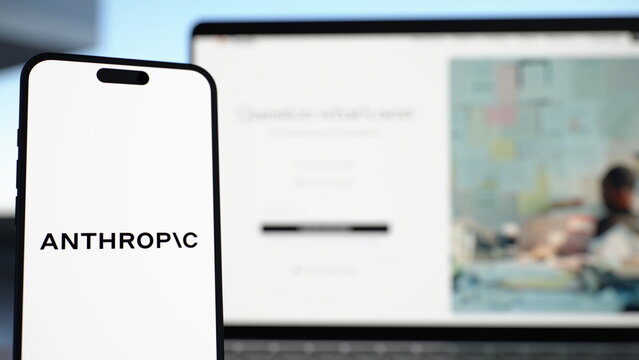 The Anthropic logo displayed on a smartphone held in front of a laptop showing the Claude website. Anthropic Launches Claude Haiku 5.5 for Fast, Low-Cost AI Tasks. October 7, 2026, Lisbon, Portugal.