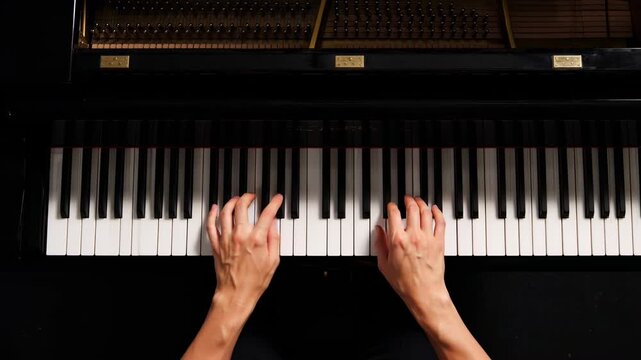 Top down view of musician hands playing black grand piano during performance.